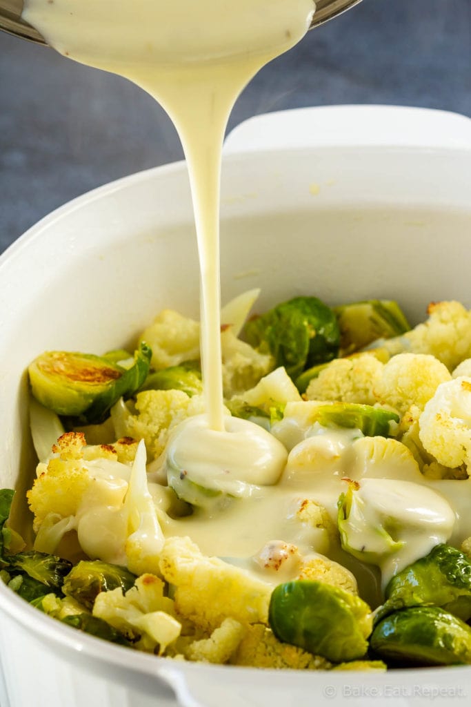 Homemade cheese sauce pouring onto roasted brussel sprouts and cauliflower
