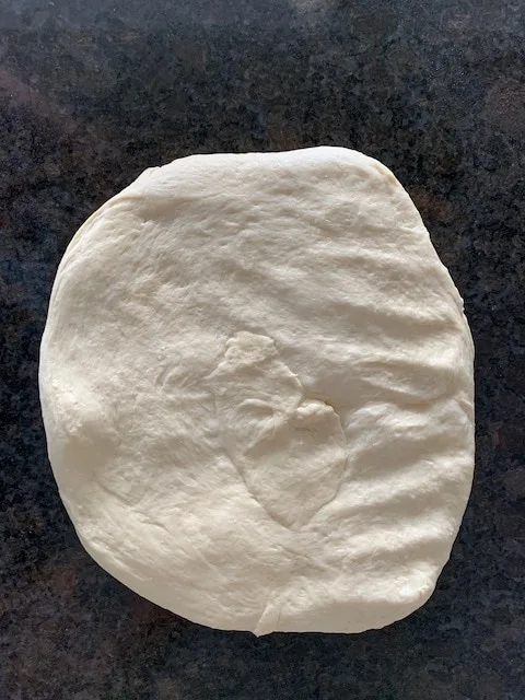 Bread dough pressed out into a thick rectangle to start shaping it into a loaf.