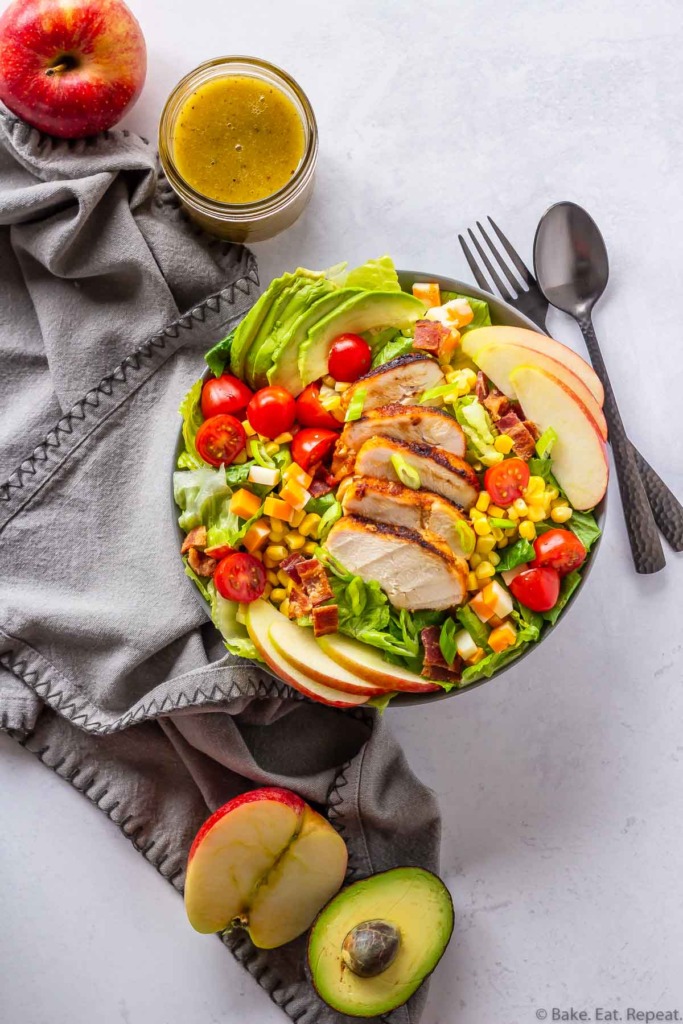 Dinner salad with apples, tomatoes, corn, cheese, green onions, avocado, grilled chicken, and a honey mustard salad dressing