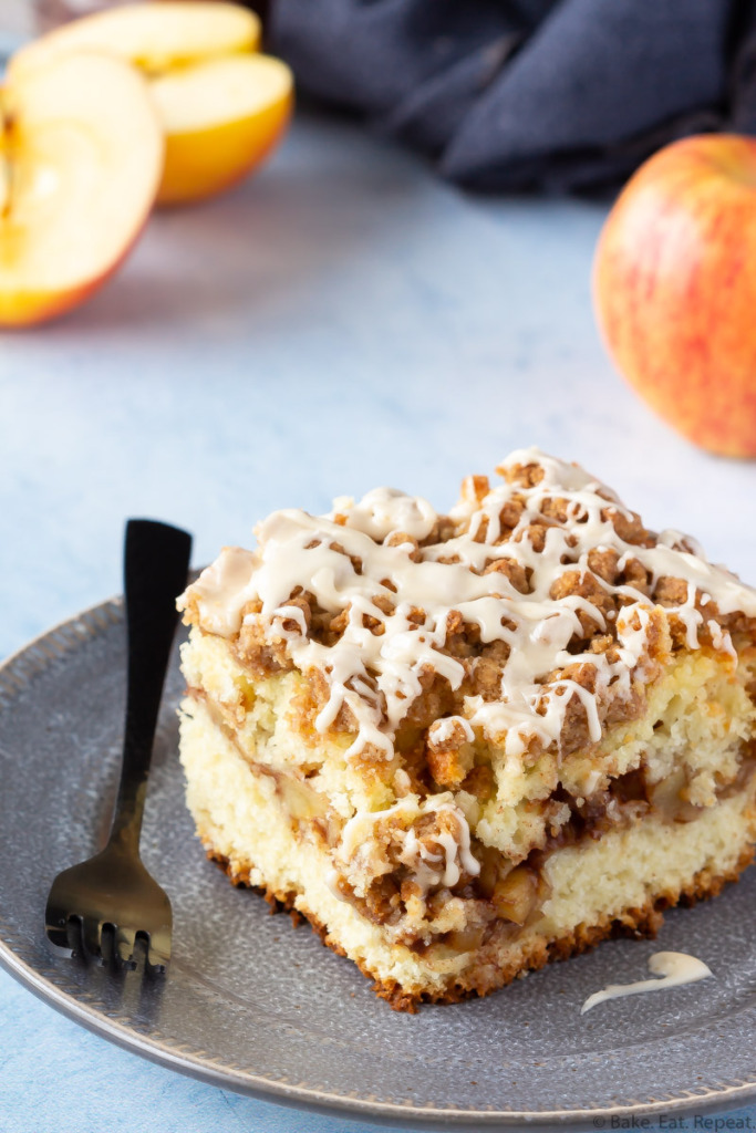 Piece of apple cinnamon filled coffee cake with a crumb topping and a salted caramel glaze on a place with apples.