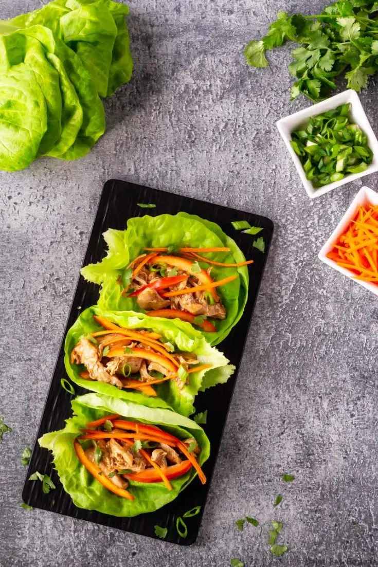 Hoisin chicken lettuce wraps on a platter with carrots, lettuce, cilantro and green onions.