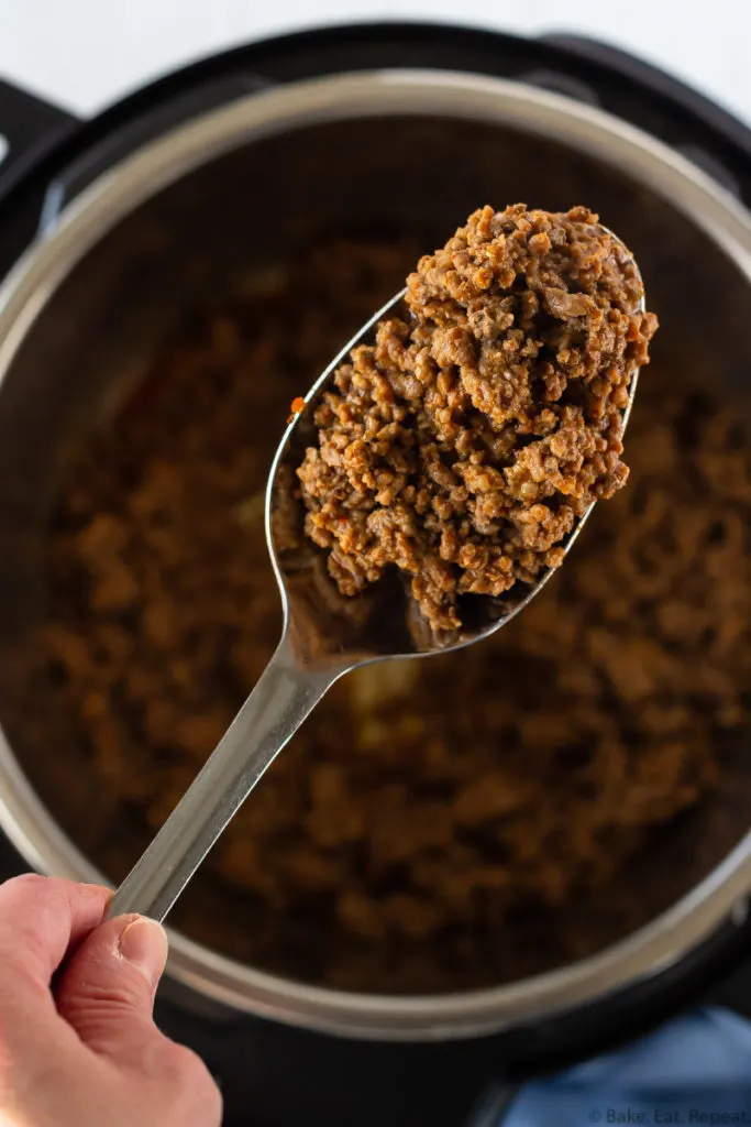 Taco meat in a spoon held above the Instant Pot that it was cooked in from frozen ground beef.